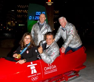 Gold Medal winner Maelle Ricker, and OMEGA President Stephen Urquhart in bobsleight, standing in the back is Astronaut Tom Stafford and in the back is Astronaut Gene Cernan