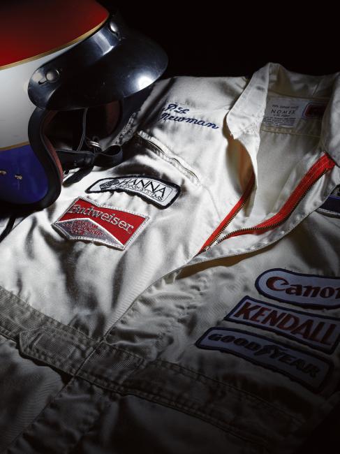 The white suit with red and blue stripes is presented with a red, white and blue helmet, accompanied by copies of photographs showing Newman wearing the suit and helmet and a letter of authenticity written by P. Avanzato, a fabricator at Bob Sharp Racing from 1972 to 1987.