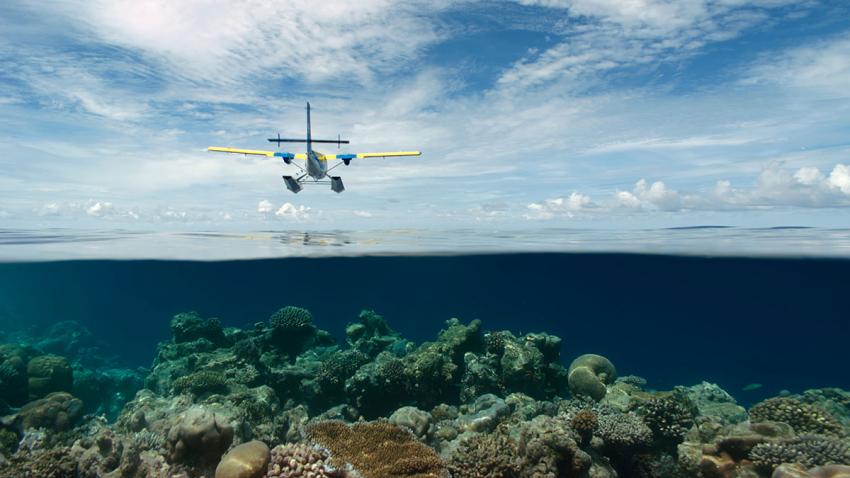 Twin Otter seaplane flying over the shallow waters of the Maldives.